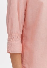 Blusa rosa a maniche corte in tessuto texture. Presenta polsini elasticizzati per una vestibilità regolabile e un sottile motivo orizzontale.