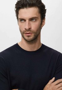 Suéter de cuello redondo en color navy, con un diseño ajustado fabricado en un tejido de punto suave, que presenta puños y dobladillo acanalados, creando una silueta limpia.