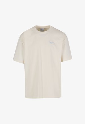 Kermainen puuvillainen t-paita, jossa on pyöreä pääntie ja lyhyet hihat, vasemmassa rinnassa pieni sininen kirjailtu logo.