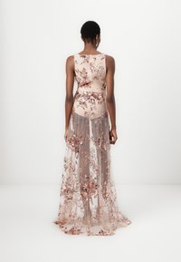 Μακρύ φόρεμα με λουλουδάτο σχέδιο σε απαλή ροζ απόχρωση με διάφανο επικάλυμμα. Διαθέτει λεπτομέρειες με παγιέτες και εφαρμοστό κορσέ, ρέει σε στρωτή φούστα.