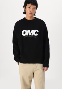 Suéter negro de canalé con logo blanco "OMC" y el texto "OFF-TRACK MEMBERS' CLUB". Corte relajado con mangas largas y escote redondo.