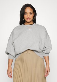 Felpa grigia con una vestibilità rilassata e spalle a caduta, con polsini a coste. Abbinata a una gonna beige plissettata e catene sovrapposte.