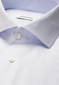 Chemise blanche à motif de traits diagonaux bleu clair, col boutonné et étiquette de marque "seidensticker" visible à l'intérieur du col.
