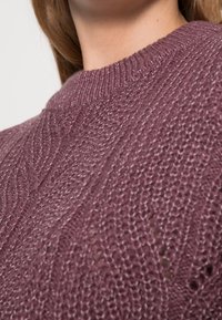 Knitted sweater in soft, textured yarn. Features a round neckline and a rich mauve color with a cable pattern throughout.