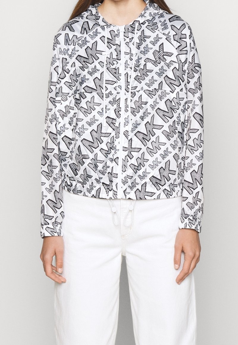 Biała krótka kurtka z czarnym wzorem graficznym z logo "MK", zamek błyskawiczny z przodu oraz regulowany ściągacz u dołu i przy rękawach.