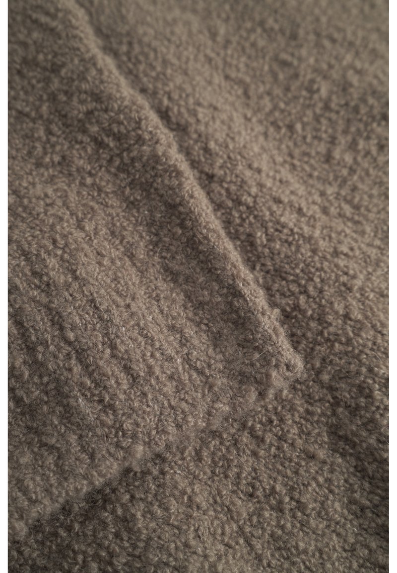 Tissu brun, texturé, avec une apparence douce et duveteuse. Le matériau présente un motif côtelé, indiquant un design tricoté ou tissé.
