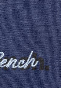 Blauer Strickstoff mit besticktem Text. Das Wort "Französisch." ist in hellblauen und schwarzen Buchstaben mit einer strukturierten Oberfläche dargestellt.