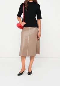 Haut noir à manches courtes côtelé, jupe midi en cuir beige avec détails de coutures, escarpins noirs à bout pointu, et petit sac à main rouge.