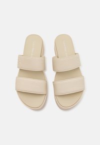 Sandali scivolati beige con due ampie cinghie in tessuto, soletta morbida e design minimalista. Il marchio è impresso sulle cinghie.