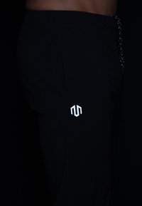 Schwarze Sporthose mit elastischem Bund, Kordelzug und einem kleinen weißen Logo an der Seite. Glattes, leichtes Material.