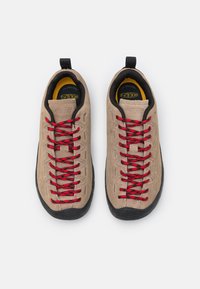 Chaussons d'escalade beige avec des lacets rouges et des semelles en caoutchouc noir, dotés d'un dessus texturé et d'une languette au talon pour un enfilage facile.
