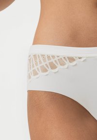 Witte slip gemaakt van zacht materiaal. Beschikt over een kantafwerking met een diamanten patroon op de taille, wat textuur en detail toevoegt.
