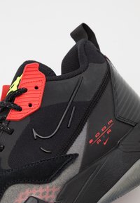 Gros plan d'une chaussure Nike Zoom Air noire avec des touches rouges et jaune fluo et une semelle texturée.