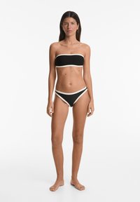 Črn bandeau bikini z kontrastnimi kremnimi poudarki, ki se ponaša z gladko teksturo in prilegajočo zasnovo za poenoteno silhueto.