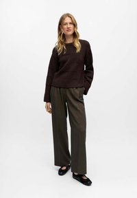 Bruine textuursweater met een boxy pasvorm, gecombineerd met hoge, wijde, donkergroene broek en zwarte instap schoenen.