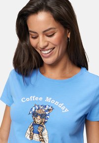 T-shirt en coton bleu avec un léopard portant des lunettes de soleil et un bandeau rayé, tenant une tasse de café, avec le texte "Coffee Monday".