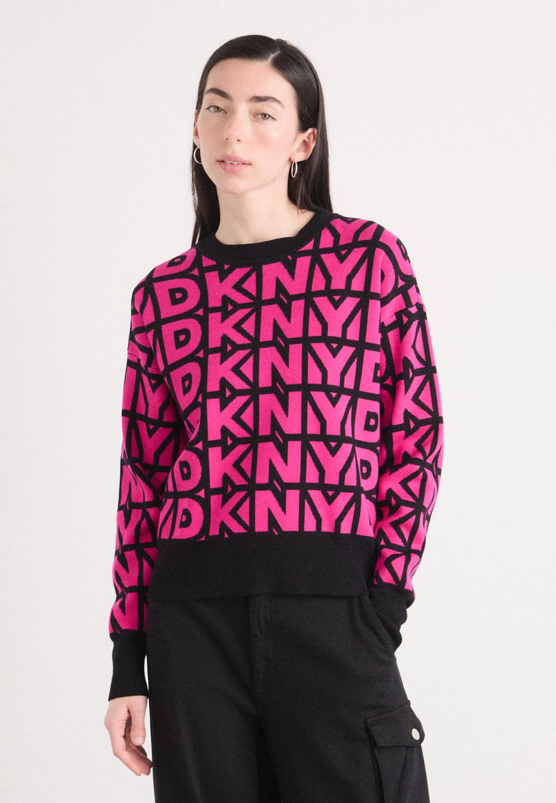 Różowy sweter z dzianiny z wyraźnym czarnym wzorem graficznym z logo "DKNY". Posiada okrągły dekolt i ściągacze na mankietach, wykonany z miękkiego materiału.