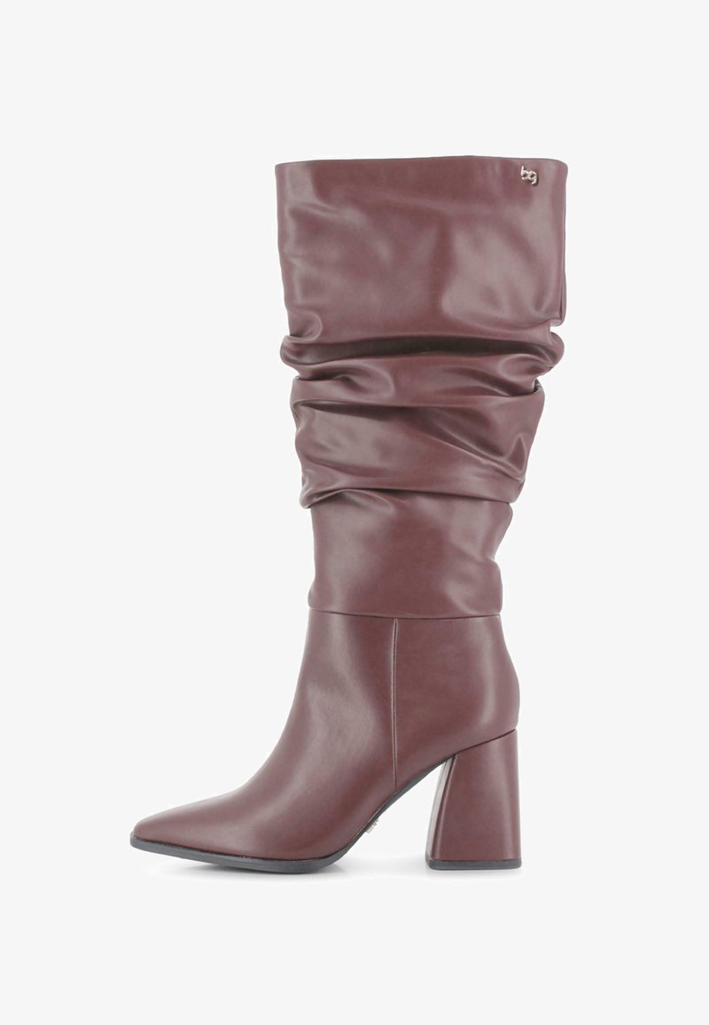 Bota de cuero marrón hasta la mitad de la pantorrilla, con un tacón grueso y punta afilada, que presenta un pequeño logo metálico cerca de la parte superior.