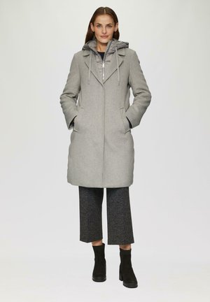 Manteau en mélange de laine gris avec capuche zippée, poches avant et design structuré. Pantalons cropped noirs texturés et bottes noires à la cheville.
