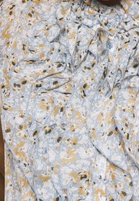 Blusa azul clara con un patrón floral en amarillo y verde. Presenta detalles con volantes, botones y una textura sutil.