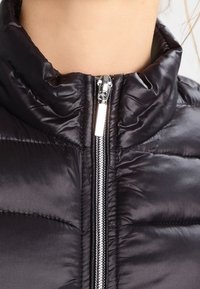 Czarna kurtka puchowa z wysokim kołnierzem, zapięciem na srebrny suwak i pikowaną fakturą, wykonana z błyszczącego, lekkiego materiału.