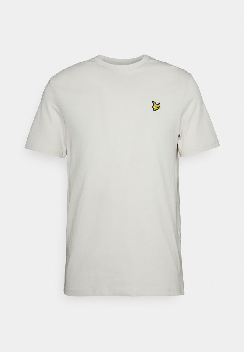 Camiseta de manga corta en color crema, de algodón, con cuello redondo y un pequeño logo de mariposa bordado en amarillo en el pecho.