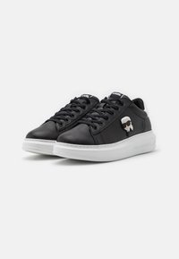 Zwarte leren sneakers met een witte zool, voorzien van ronde veters en een cartoonlogo. Ronde neus en tekstuurdetail aan de zijkant.