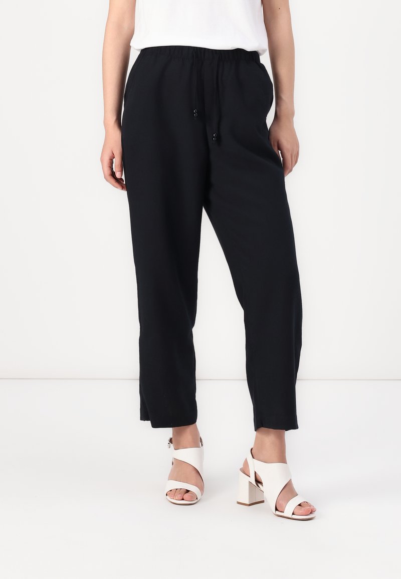 Pantaloni neri, comodi e larghi, con una vita elastica, cordoncino e orli cropped, abbinati a sandali con tacco bianchi.