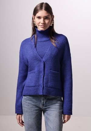 Cardigan bleu vibrant avec un col haut, des poignets côtelés et deux poches avant ; il comprend une fermeture à boutons et un tissu tricoté texturé.