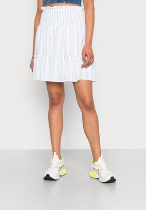 Saia branca em camadas com um cós franzido, apresentando um padrão texturizado sutil. Combinada com tênis brancos e pretos que destacam acentos brilhantes.