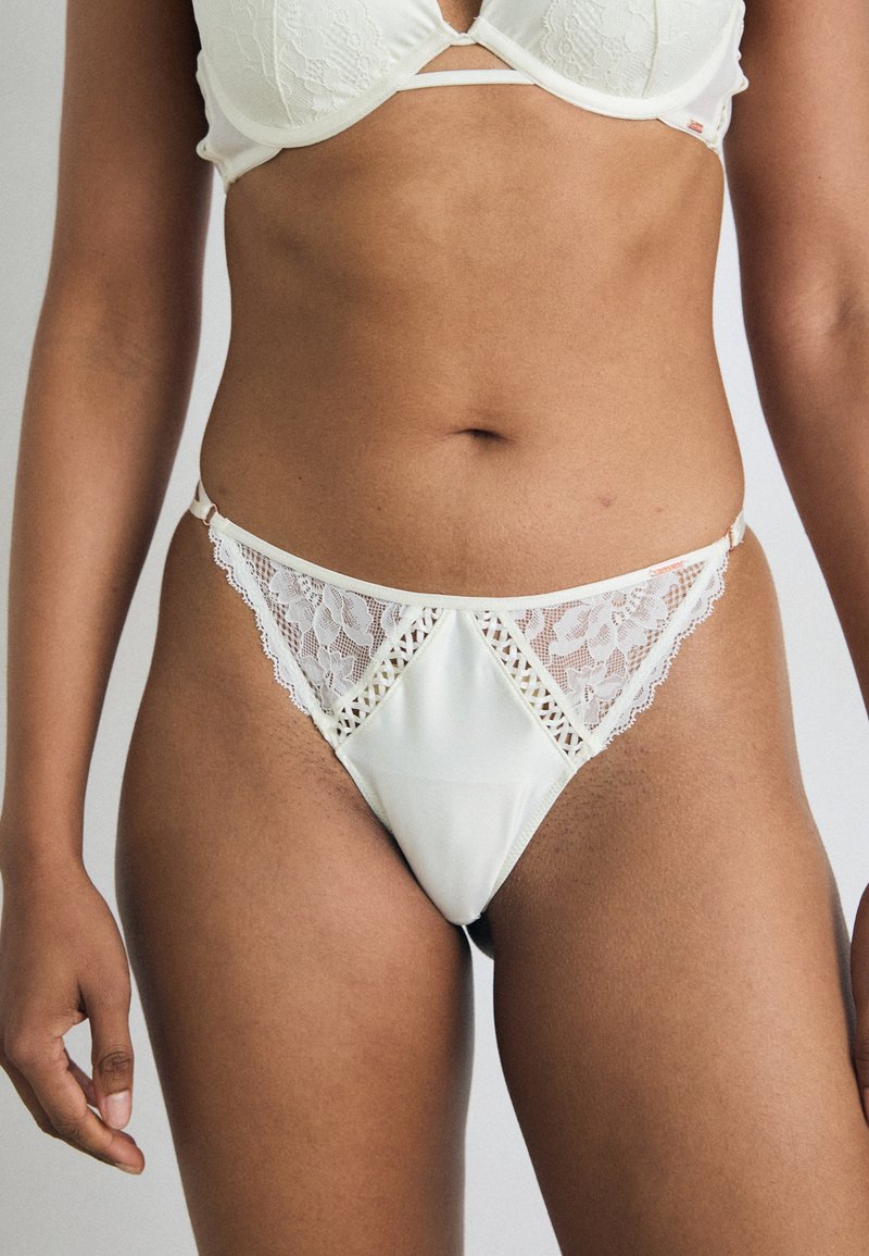 String en dentelle et satin pour femmes en crème, avec un centre en forme de diamant et des accents en dentelle délicate sur les côtés pour un design raffiné.