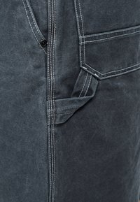 Σκούρο μπλε ύφασμα με λευκά γαζιά, που διαθέτει κλείσιμο με κουμπί, μεγάλη τσέπη με καπάκι και λεπτομέρεια λουριού με θηλιά.