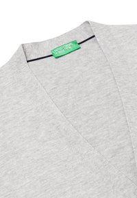 Svetle šedý pletený svetr s výstřihem do V a mírně strukturovaným povrchem. Obsahuje zelenou značkovou etiketu na výstřihu a kontrastní švové detaily.