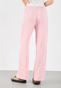 Jasnoróżowe, szerokie spodnie wykonane z teksturowanej tkaniny z pionowymi białymi paskami. Elastyczny pas, noszone z beżowymi butami.
