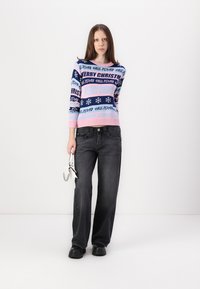 Pull tricoté en bleu, rose et blanc avec des motifs de texte et de flocons de neige. Associé à un jean noir à jambes larges et des chaussures noires épaisses.