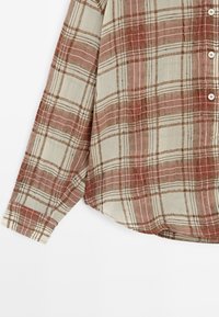 Karierte Button-Down-Bluse in hellbeige mit rot-braunem Karo-Muster; verfügt über lange Ärmel, abgerundeten Saum und feine Textur.