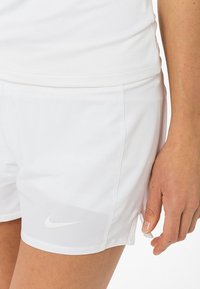 Pantalones cortos deportivos blancos de Nike hechos de tela ligera. Presentan aberturas laterales y un pequeño logo blanco de Nike en el dobladillo inferior.