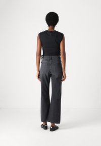 Black cropped top and high-waisted, wide-leg jeans in dark denim, featuring two back pockets and a raw hem. Smooth texture with minimal stitching.
