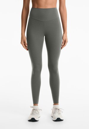Leggings taille haute et moulants en tissu gris atténué avec une texture lisse. Associés à des chaussures de sport de couleur claire.