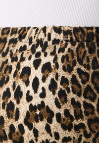 Tkanina s leopardjim vzorcem na bežnem ozadju, ki ima črne in rjave lise, z nabranim elastičnim pasom za varno prileganje.