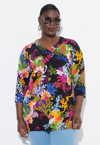 Svart blommig tunika med livfulla flerfärgade mönster, 3/4-ärmar och V-ringning, i kombination med ljusblå byxor.