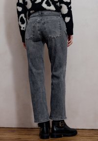 Jeans grigi alti in vita con taglio diritto, dotati di tasche posteriori e una texture in denim. Indossati con stivaletti alla caviglia in pelle nera.