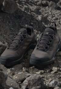 Para czarnych i ciemnoszarych butów trekkingowych z teksturowanymi podeszwami umieszczona na skalistym terenie na zewnątrz.