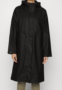 Impermeable negro con capucha, cintura ajustable con cordón y botones de presión. Presenta mangas largas y una textura suave y resistente al agua.