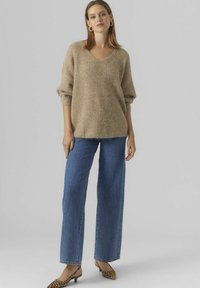 Beige stickad tröja med V-ringning och lösa ärmar, matchad med vida blå jeans. Accenterad med klackar i leopardmönster.