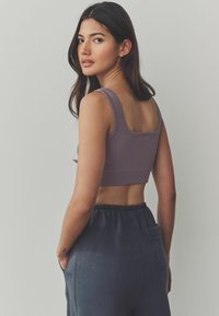 Rebrasti lavanda crop top s širokim trakama, uparen s tamnoplavim hlačama s elastičnim pojasom i bočnim džepovima. Minimalistički dizajn, mekani materijal.