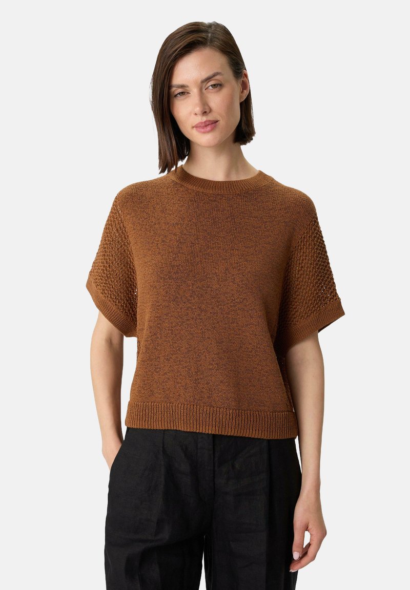 Brauner gestrickter Pullover mit kurzen Ärmeln, einem gerippten Saum und strukturierten Schultern, kombiniert mit schwarzen Hosen.