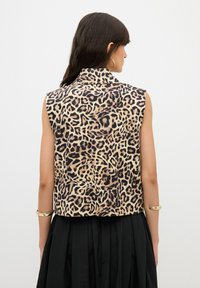 Mouwloze top met luipaardprint en kraag, gemaakt van een zachte stof met een gladde textuur, gecombineerd met een zwarte rok.