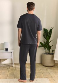 Czarny szary zestaw bawełnianych koszulki i spodni, luźny krój, krótkie rękawy, minimalistyczny design, zestawiony z rośliną i lampą w neutralnym pomieszczeniu.