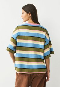 Proužkované nadměrné tričko v modré, zelené a růžové barvě; krátké rukávy; kulatý výstřih; měkká textura; ve spojení s hnědými manšestrovými kalhotami.